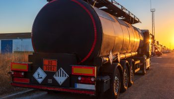 Black tanker truck for the transport of dangerous goods, in front of a street at sunset.
